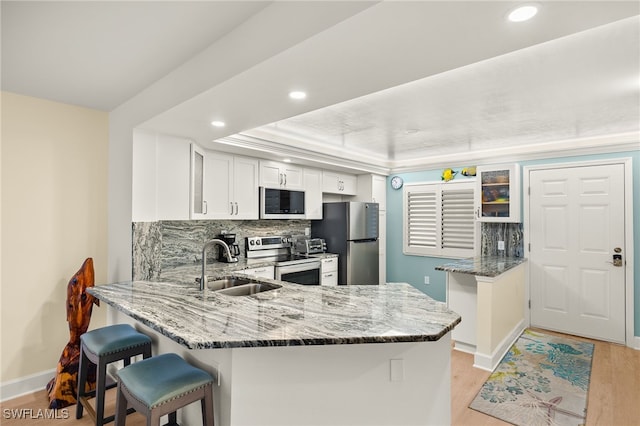 kitchen featuring light wood finished floors, stone countertops, appliances with stainless steel finishes, a peninsula, and a sink