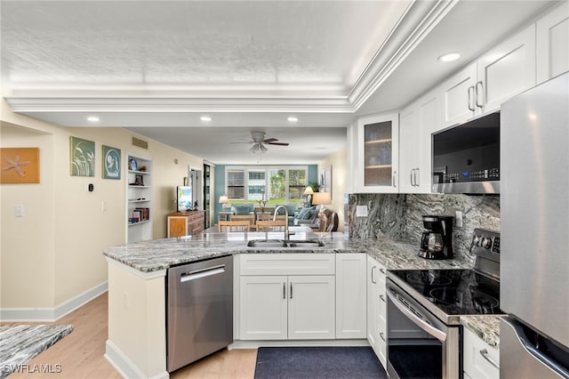 kitchen featuring white cabinets, glass insert cabinets, appliances with stainless steel finishes, a peninsula, and a sink