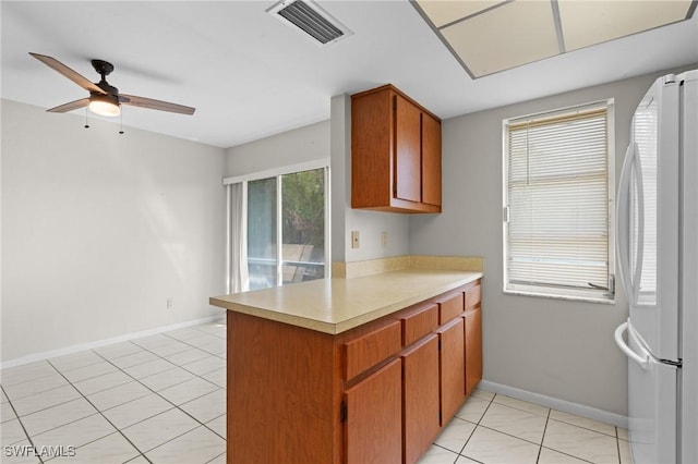 kitchen with light tile patterned floors, a peninsula, visible vents, light countertops, and freestanding refrigerator