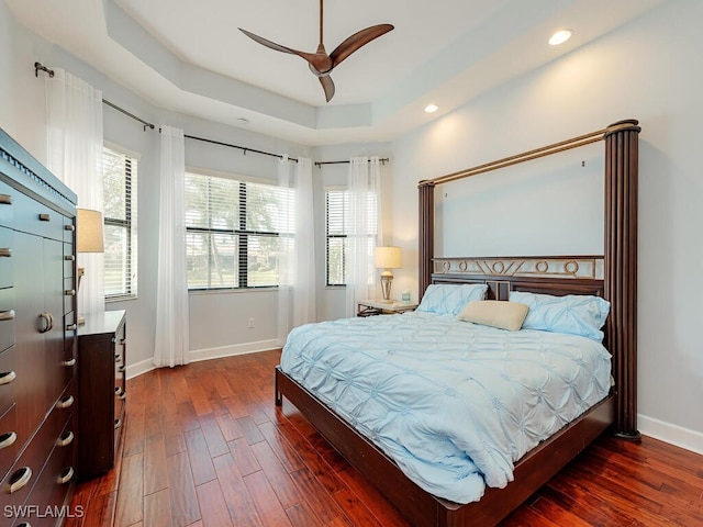 bedroom with baseboards, a ceiling fan, dark wood-style flooring, a tray ceiling, and recessed lighting