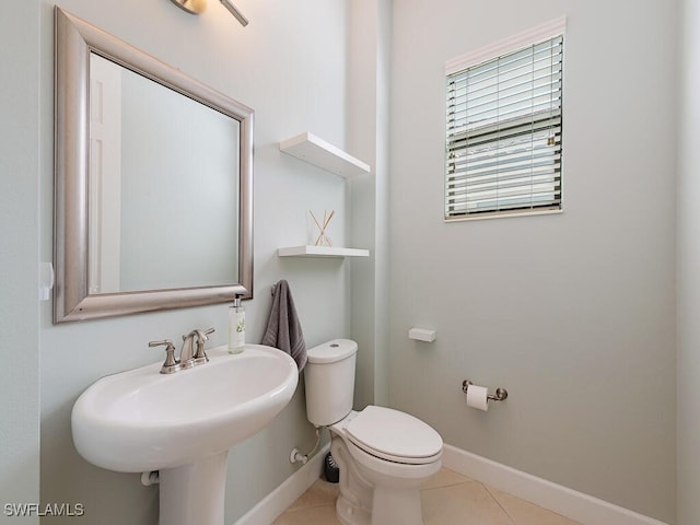 half bathroom with baseboards, toilet, and tile patterned floors