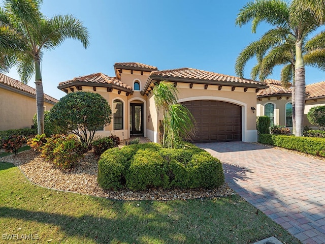 mediterranean / spanish house featuring an attached garage, a tile roof, decorative driveway, and stucco siding