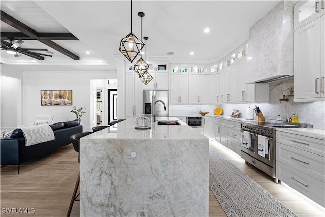 kitchen featuring a sink, open floor plan, appliances with stainless steel finishes, decorative backsplash, and wall chimney exhaust hood