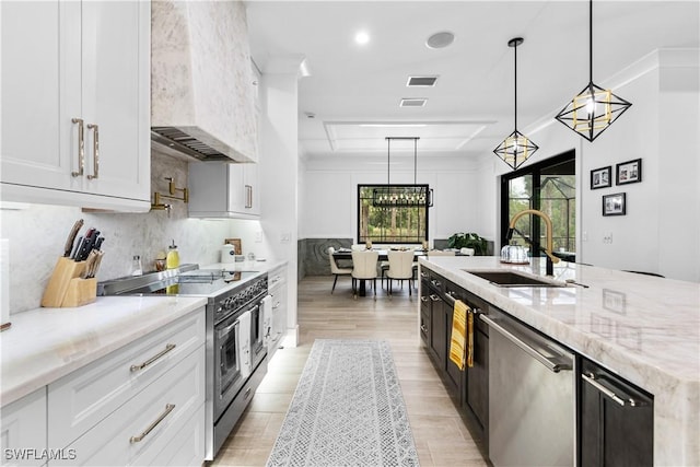 kitchen with light stone countertops, a sink, appliances with stainless steel finishes, decorative backsplash, and custom range hood