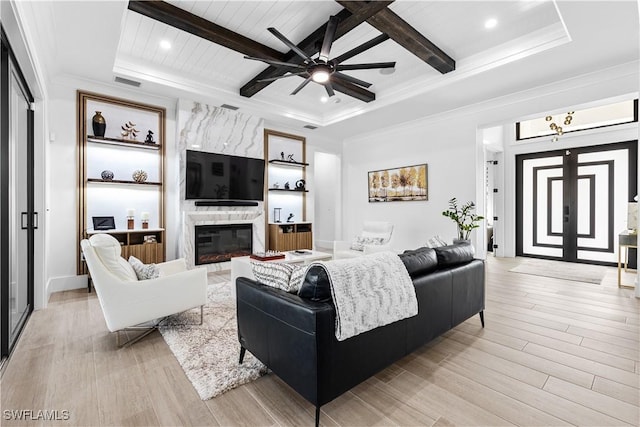 living area featuring light wood-type flooring, a fireplace, visible vents, and beam ceiling