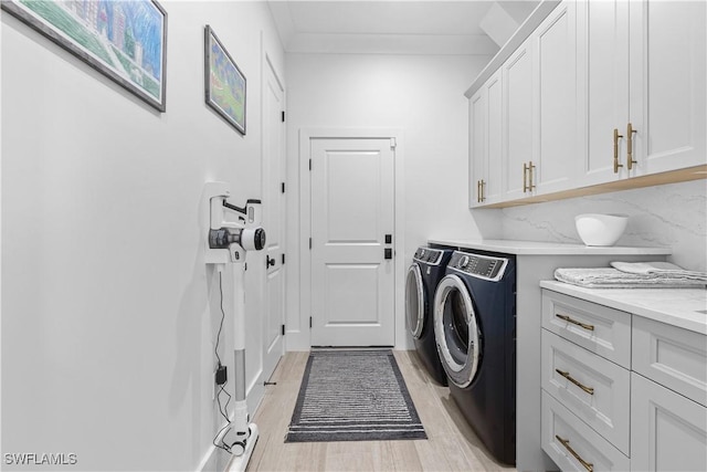 laundry room featuring ornamental molding, light wood-style flooring, washing machine and clothes dryer, and cabinet space