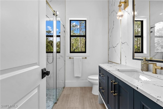 bathroom with toilet, a shower with shower door, vanity, wood finished floors, and baseboards