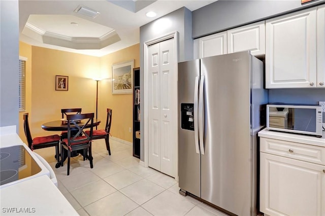 kitchen featuring a tray ceiling, crown molding, light tile patterned floors, white cabinets, and stainless steel fridge