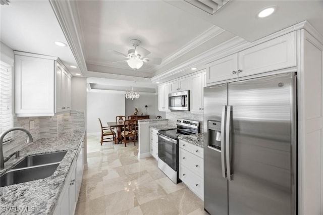 kitchen with a tray ceiling, stainless steel appliances, ornamental molding, white cabinetry, and a sink