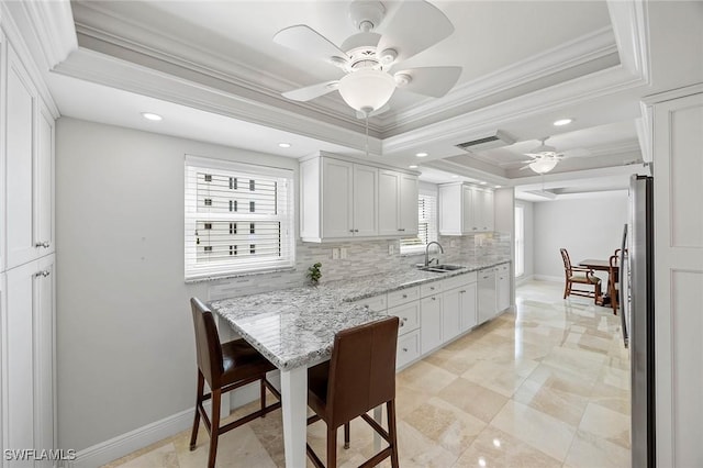 kitchen featuring freestanding refrigerator, a raised ceiling, white cabinetry, and a sink