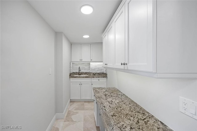 kitchen featuring light stone countertops, decorative backsplash, white cabinets, and a sink