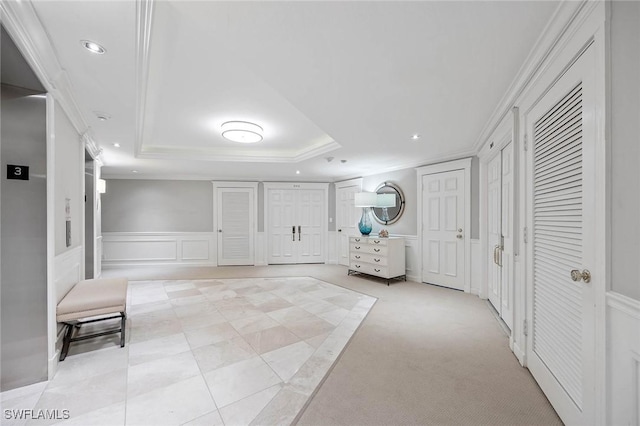 hallway featuring crown molding, a wainscoted wall, a raised ceiling, and a decorative wall