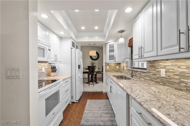 kitchen featuring white appliances, a sink, white cabinets, ornamental molding, and a raised ceiling