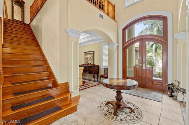 entryway with decorative columns, arched walkways, ornamental molding, stairs, and light tile patterned flooring