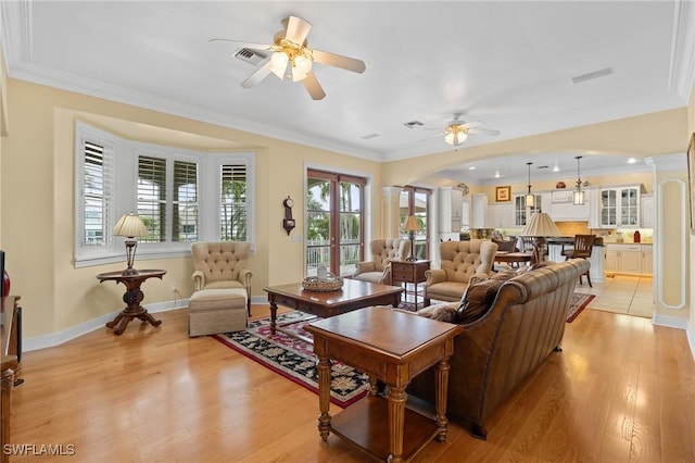 living area with ornamental molding, arched walkways, visible vents, and light wood-style flooring