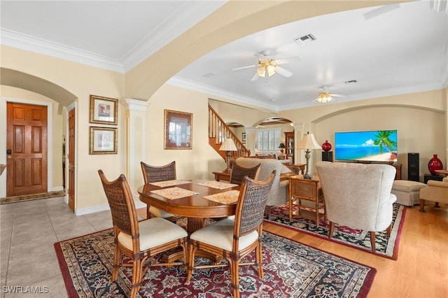 dining room with arched walkways, ceiling fan, stairs, ornamental molding, and decorative columns