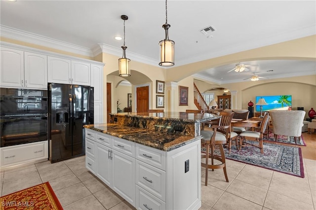 kitchen featuring light tile patterned floors, arched walkways, a kitchen island, a ceiling fan, and black appliances