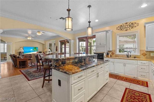 kitchen featuring arched walkways, decorative columns, open floor plan, a kitchen island, and a sink