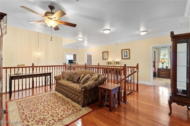 living area featuring ceiling fan with notable chandelier, crown molding, baseboards, and wood finished floors