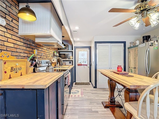 kitchen with brick wall, appliances with stainless steel finishes, wood counters, and light wood-style flooring