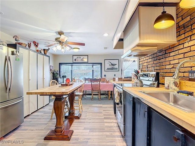 kitchen with appliances with stainless steel finishes, wooden counters, light wood finished floors, and a sink