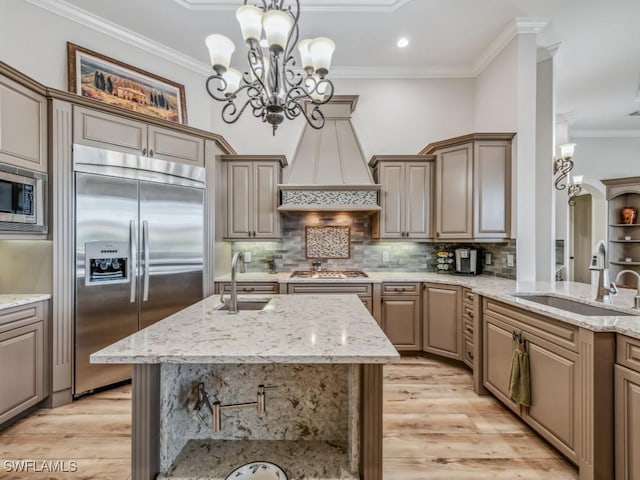 kitchen with ornamental molding, light stone countertops, built in appliances, and a sink