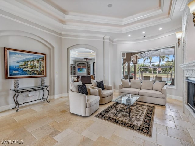 living room featuring baseboards, a raised ceiling, stone tile flooring, and a fireplace