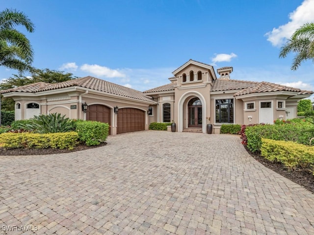 mediterranean / spanish house with stucco siding, a tile roof, decorative driveway, french doors, and a garage