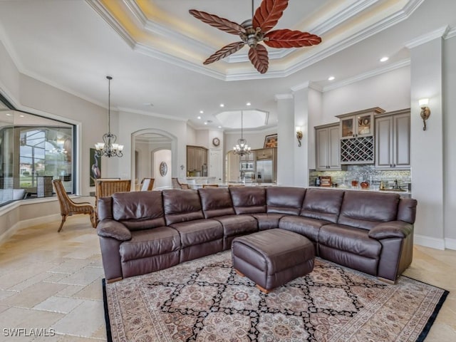 living room with baseboards, a tray ceiling, arched walkways, stone tile flooring, and ceiling fan with notable chandelier