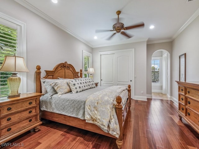 bedroom with crown molding, baseboards, dark wood-style floors, arched walkways, and a closet