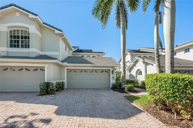 view of home's exterior with a tile roof, decorative driveway, an attached garage, and stucco siding