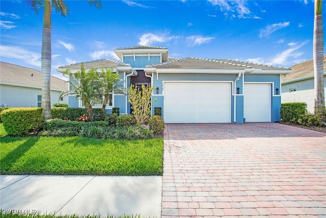 view of front facade with a tiled roof, a front yard, decorative driveway, and a garage