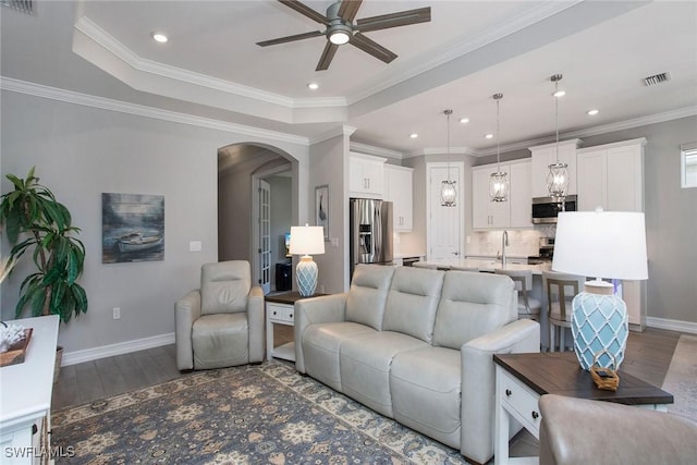 living room featuring visible vents, ornamental molding, wood finished floors, arched walkways, and baseboards