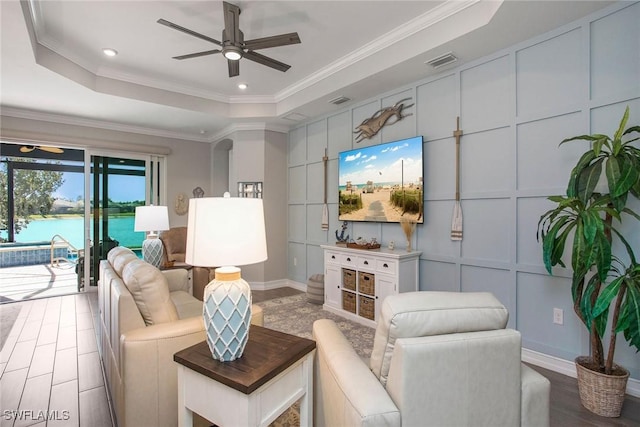 living room with visible vents, ornamental molding, wood finished floors, a decorative wall, and a raised ceiling