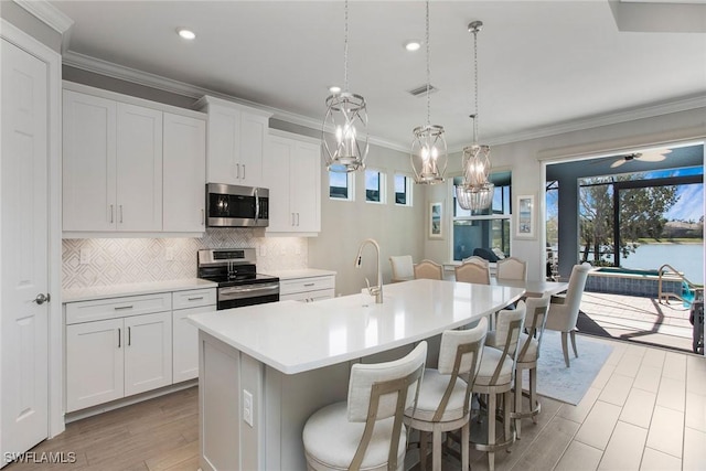 kitchen featuring visible vents, a center island with sink, ornamental molding, appliances with stainless steel finishes, and backsplash