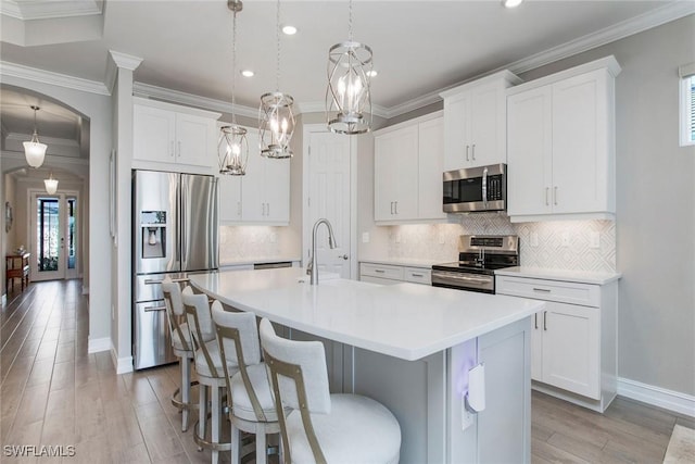 kitchen with a center island with sink, light countertops, light wood-style floors, arched walkways, and stainless steel appliances