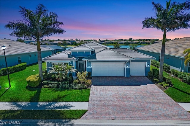 view of front facade featuring stucco siding, a front lawn, a tile roof, decorative driveway, and an attached garage