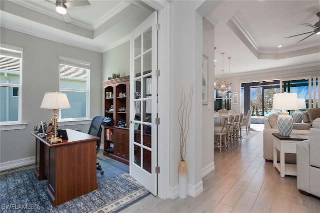 office featuring wood finished floors, baseboards, crown molding, a raised ceiling, and ceiling fan with notable chandelier