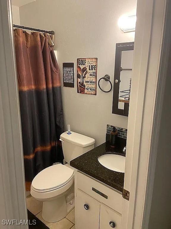 bathroom with toilet, curtained shower, tile patterned flooring, and vanity