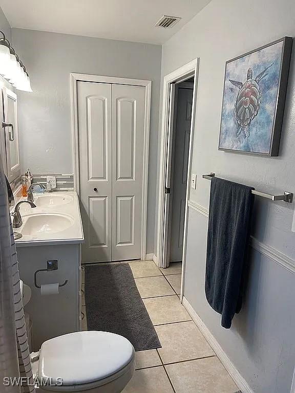 bathroom with a sink, visible vents, baseboards, tile patterned floors, and double vanity