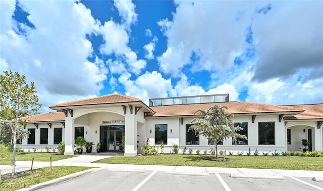 exterior space with stucco siding, a lawn, uncovered parking, and a tile roof