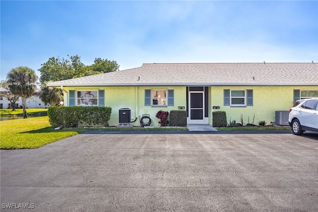 single story home with a shingled roof, a front yard, cooling unit, and stucco siding