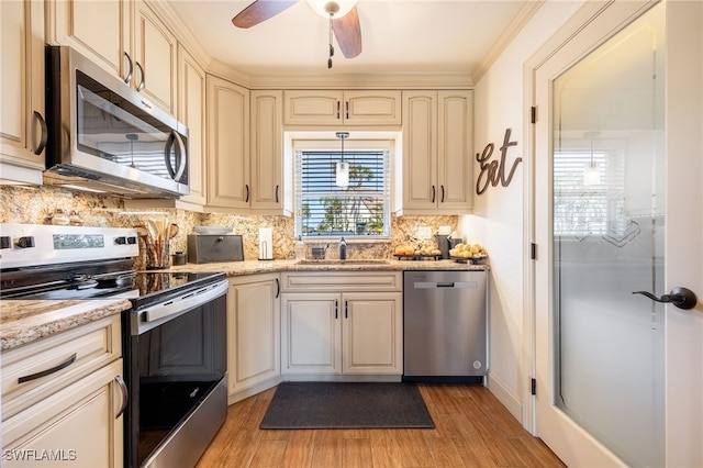 kitchen with tasteful backsplash, light wood-style flooring, appliances with stainless steel finishes, cream cabinets, and a sink