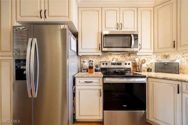 kitchen featuring appliances with stainless steel finishes, cream cabinets, light stone countertops, and decorative backsplash