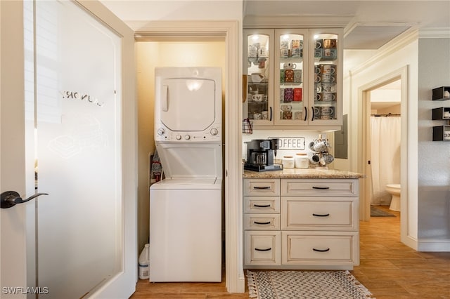 clothes washing area featuring laundry area, crown molding, light wood-style floors, and stacked washer / drying machine