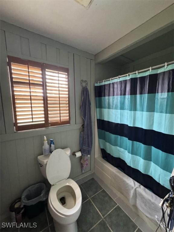 bathroom with toilet, shower / tub combo, tile patterned flooring, and a decorative wall