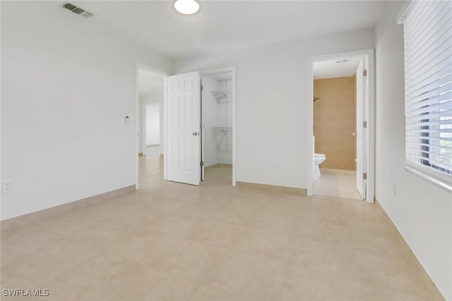 unfurnished bedroom with baseboards, visible vents, ensuite bathroom, a walk in closet, and a closet