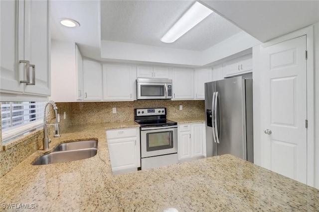 kitchen with a sink, white cabinets, appliances with stainless steel finishes, backsplash, and light stone countertops