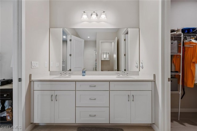 full bathroom featuring a walk in closet, a sink, baseboards, and double vanity