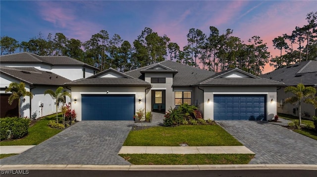 view of front facade featuring a garage, decorative driveway, a tile roof, and stucco siding